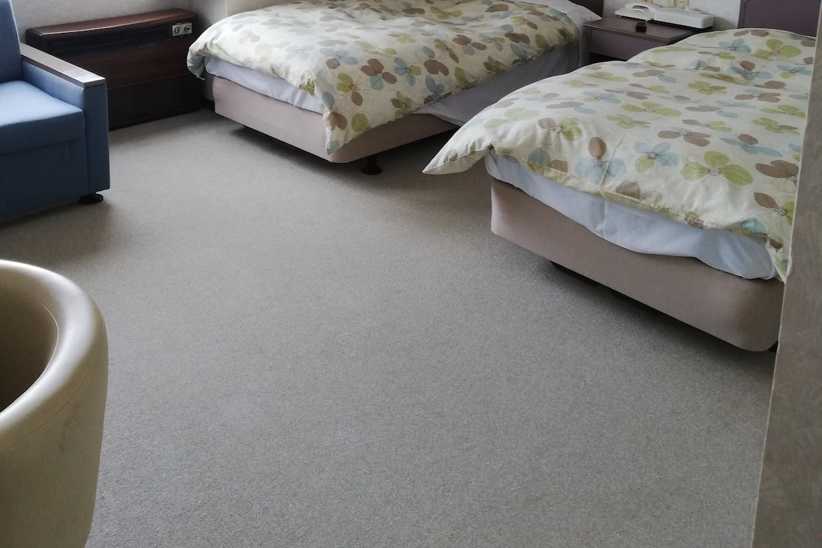 A hotel room with two beds, a desk, a chair, and a window with curtains.