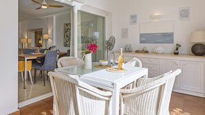 Een eetruimte met een glazen tafel, rieten stoelen en uitzicht op de keuken.