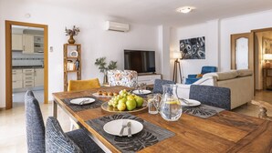 Een moderne woonkamer met een eettafel gedekt voor vier personen, een bank, een televisie en een keuken die zichtbaar is door een open doorgang.