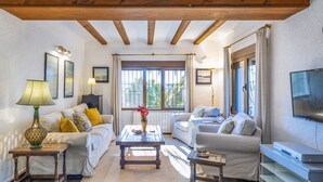 A cozy living room with two sofas, a coffee table, and a TV. There are windows with curtains, a lamp, and framed pictures on the walls. - Casa Alba (Javea / Xàbia)