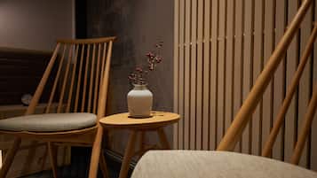 A wooden chair with a cushioned seat, a small round table with a white vase containing red berries, and a vertical wooden slat wall.