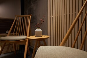 A wooden chair with a cushioned seat, a small round table with a white vase containing red berries, and a vertical wooden slat wall.