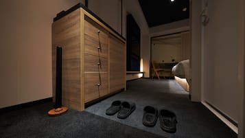 A hallway with a wooden wardrobe, a pair of slippers, and a bed in the background.