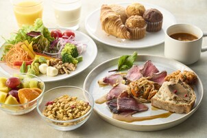 Un desayuno con platos de comida, entre ellos frutas, verduras y pasteles, además de una taza de café.