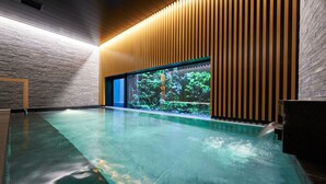 A modern indoor swimming pool with a clear view of greenery outside, wooden paneling on the walls, and a sleek, reflective pool floor. - Resol Hotel Trinity Osaka (Osaka)