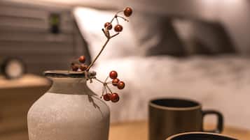A vase with red berries on a bedside table next to a bed.