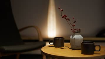 A round wooden table with two dark mugs and a clear glass jar with red berries.