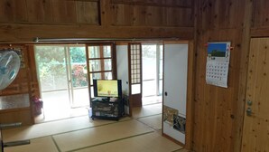 Ett traditionellt japanskt rum med tatamimattor på golvet, en tv, en kalender och en skjutdörr som leder ut till en trädgård.