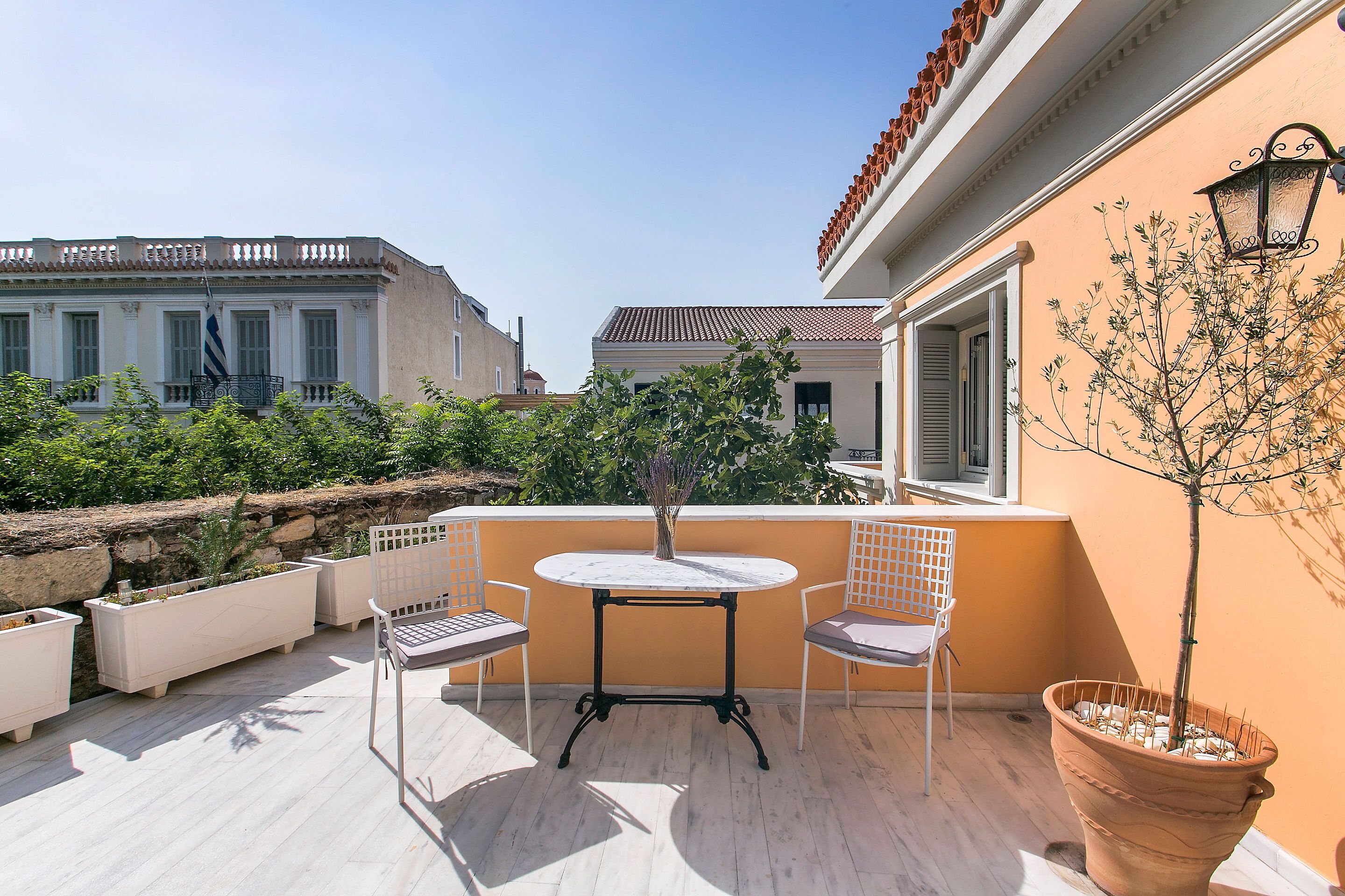 Ein Balkon mit rundem Tisch, zwei Stühlen, einem Blumentopf und Blick auf benachbarte Gebäude.
