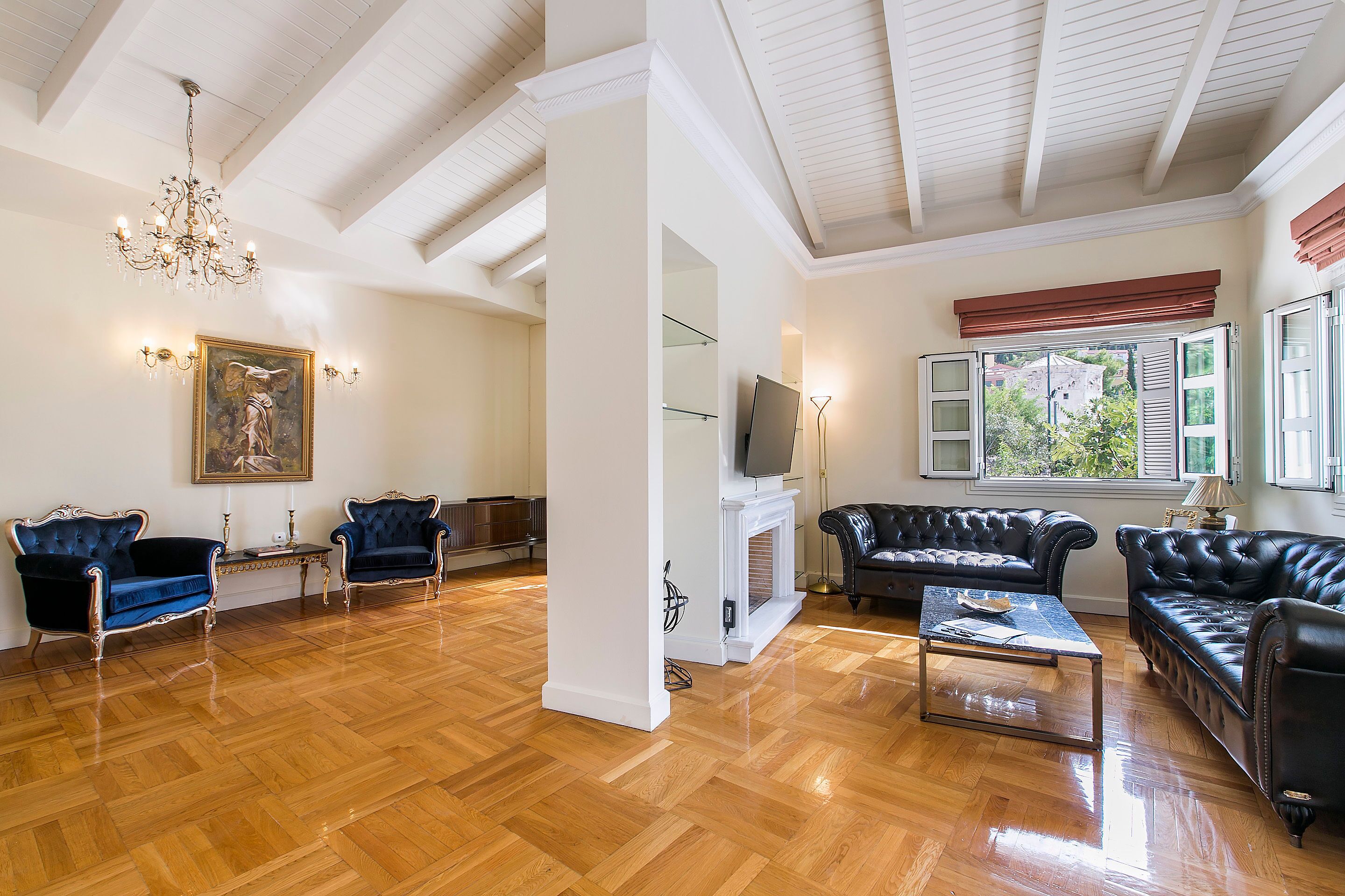 A spacious living room with hardwood flooring, a chandelier, and two black leather sofas.