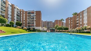 Una piscina rodeada de edificios de apartamentos con balcones, cielo despejado y algo de vegetación.