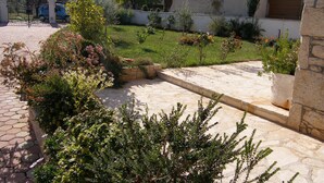 A courtyard with a stone pathway, various plants, and a building in the background. - Villa Ana - Peaceful Location (Marcana)