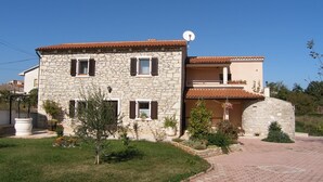 A two-story stone house with a tiled roof, a satellite dish, and a small garden with various plants and flowers. - Villa Ana - Peaceful Location (Marcana)