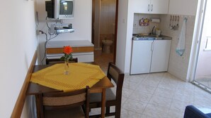 A compact kitchen with white cabinets, a small refrigerator, and a dining area with a table and chairs. - Villa Ana - Peaceful Location (Marcana)