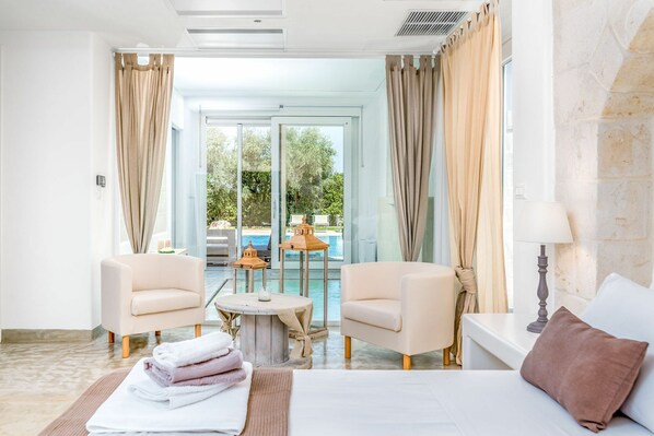 Une chambre d’hôtel comprenant un lit, deux fauteuils, une petite table ronde et donnant sur une piscine extérieure.