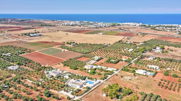 Vista aérea de una zona costera con edificios residenciales, campos de cultivo y una vista despejada del mar.