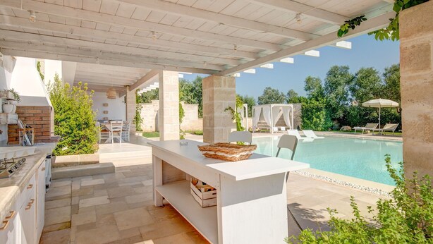 A covered outdoor area with a pool, stone pillars, and a dining setup.