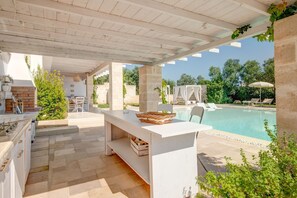 Un espacio al aire libre cubierto con una piscina, pilares de piedra y una zona de comedor.