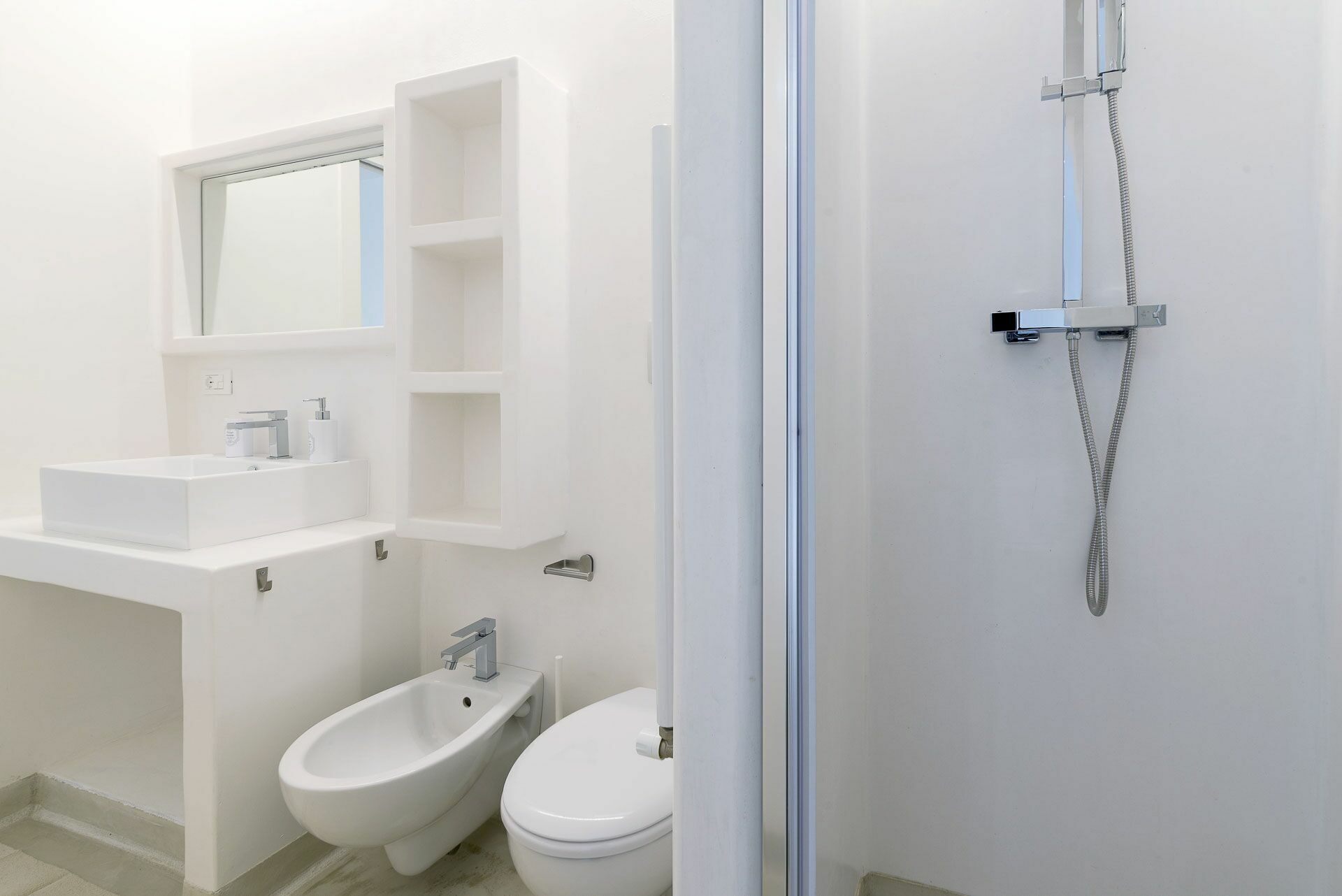 Een moderne badkamer met een wit wastafel, bidet, toilet en een douche met slang.