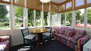 A sunroom with a round table and chairs, a striped sofa, and large windows with bamboo shades.