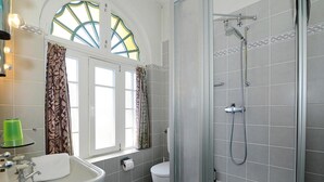 A bathroom with a sink, toilet, and shower. There is a window with curtains and a skylight.