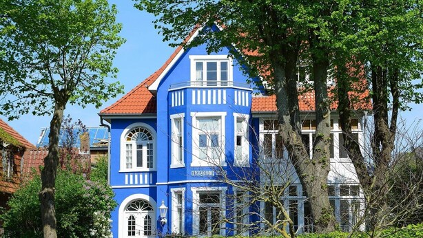 A blue building with a red roof, surrounded by trees and other buildings.