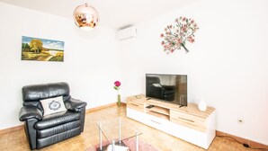 A living room with a black leather sofa, a glass coffee table, a wooden TV stand, and a floral wall decoration. - Family house with 2 apartments - Irma (Medulin)