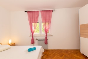 A bedroom with a bed, a nightstand, a window with pink curtains, and a radiator. - Family house with 2 apartments - Irma (Medulin)