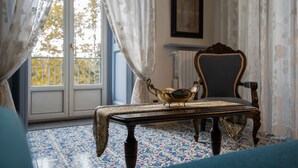 Um quarto com piso estampado, uma mesa com um objeto decorativo, uma cadeira e uma janela com cortinas.