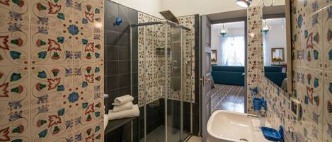Un baño con baldosas estampadas, cabina de ducha de vidrio, lavabo y espejo.