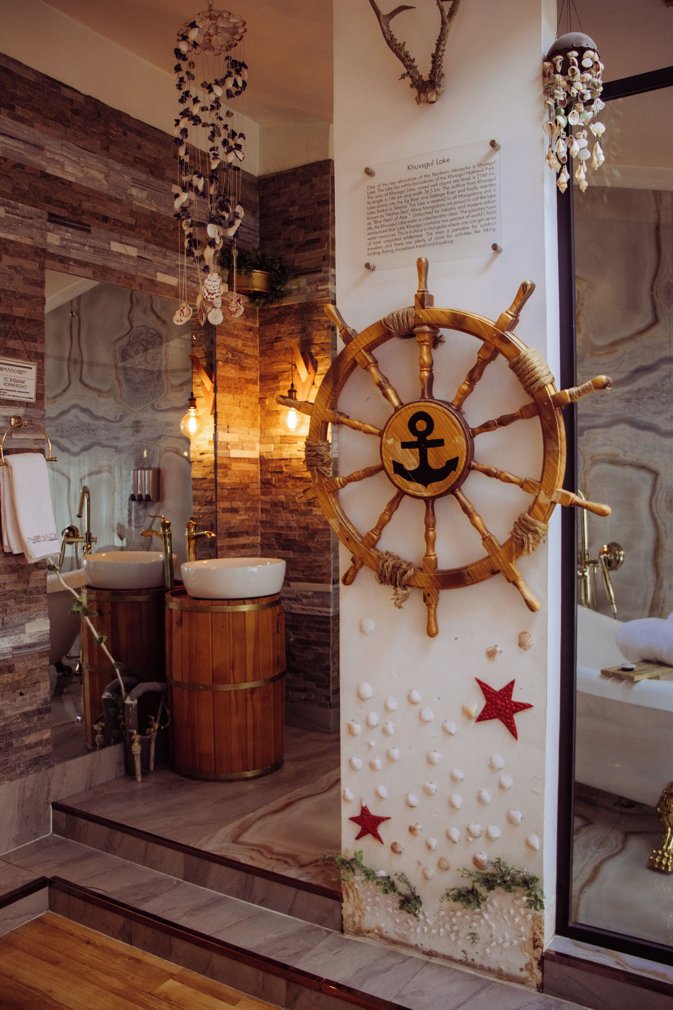 Ein Badezimmer mit einem hölzernen Steuerrad, zwei Waschbecken und einer Wand mit Muscheln und Sternen.