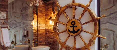 A bathroom with a wooden ship's wheel, two sinks, and a decorative wall with shells and stars.