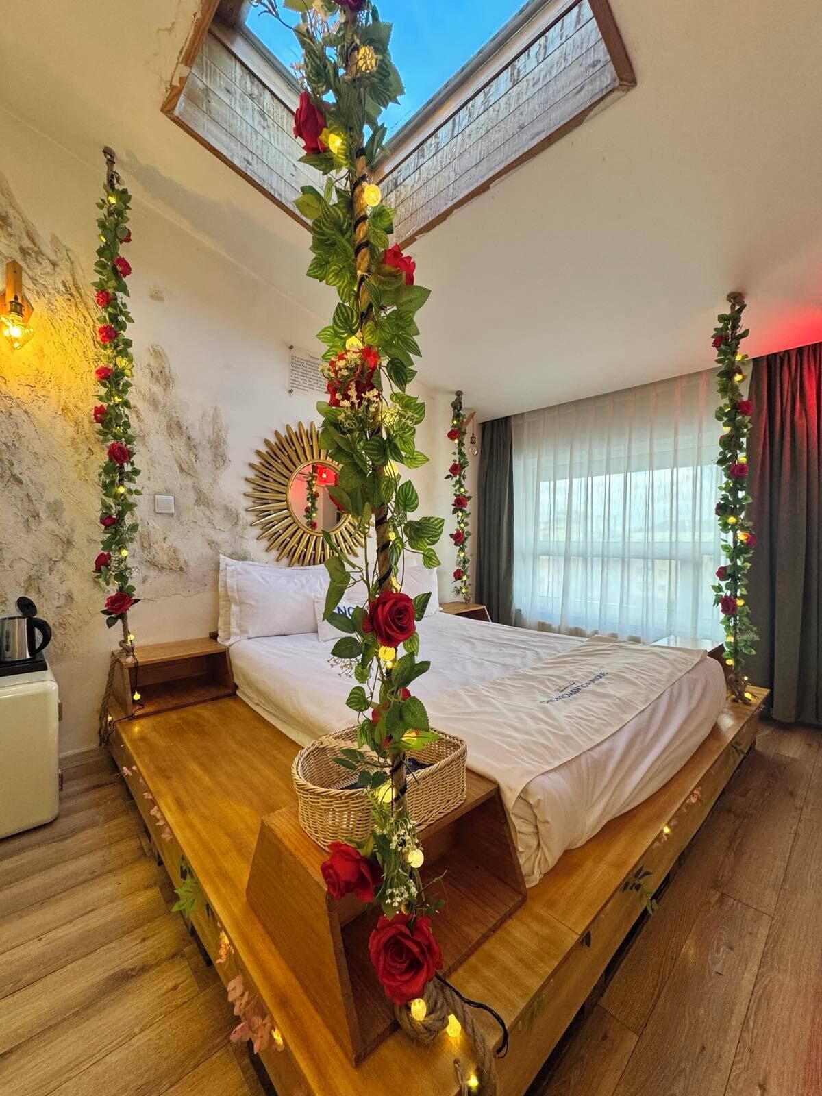 A bedroom with a bed, a wooden platform, a skylight, and a decorative plant arrangement.