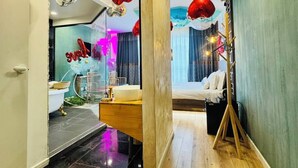 Ein modernes Hotelzimmer mit Holzboden, einem Bett, einem Schminktisch mit Spiegel und roten, kugelförmigen Leuchten.