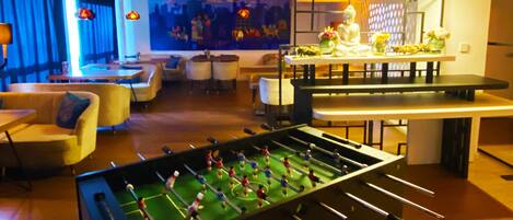 A modern indoor space with a foosball table, seating areas, and a bar.