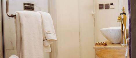 A bathroom with a glass shower enclosure, a wooden floor, a white sink with a gold faucet, and a towel rack with multiple towels.
