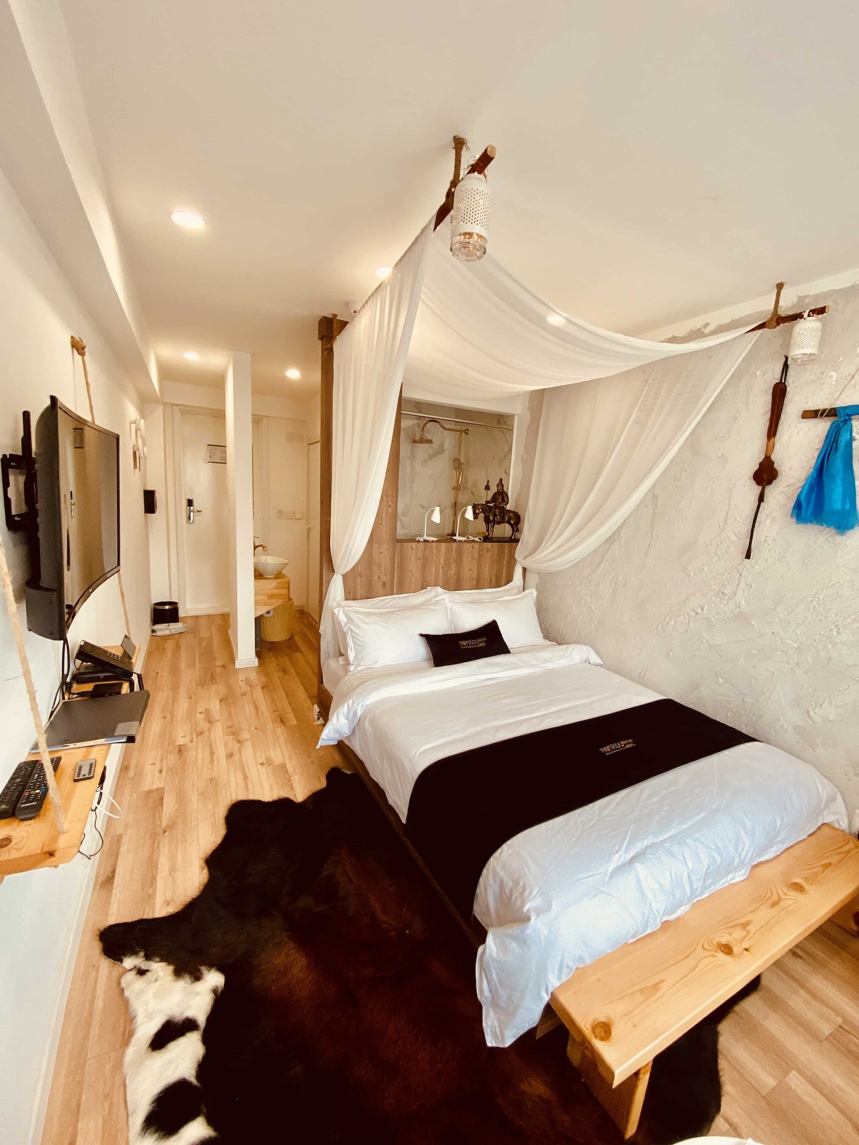 A modern bedroom with a canopy bed, a wooden bench, a cowhide rug, a mirror, and a television.