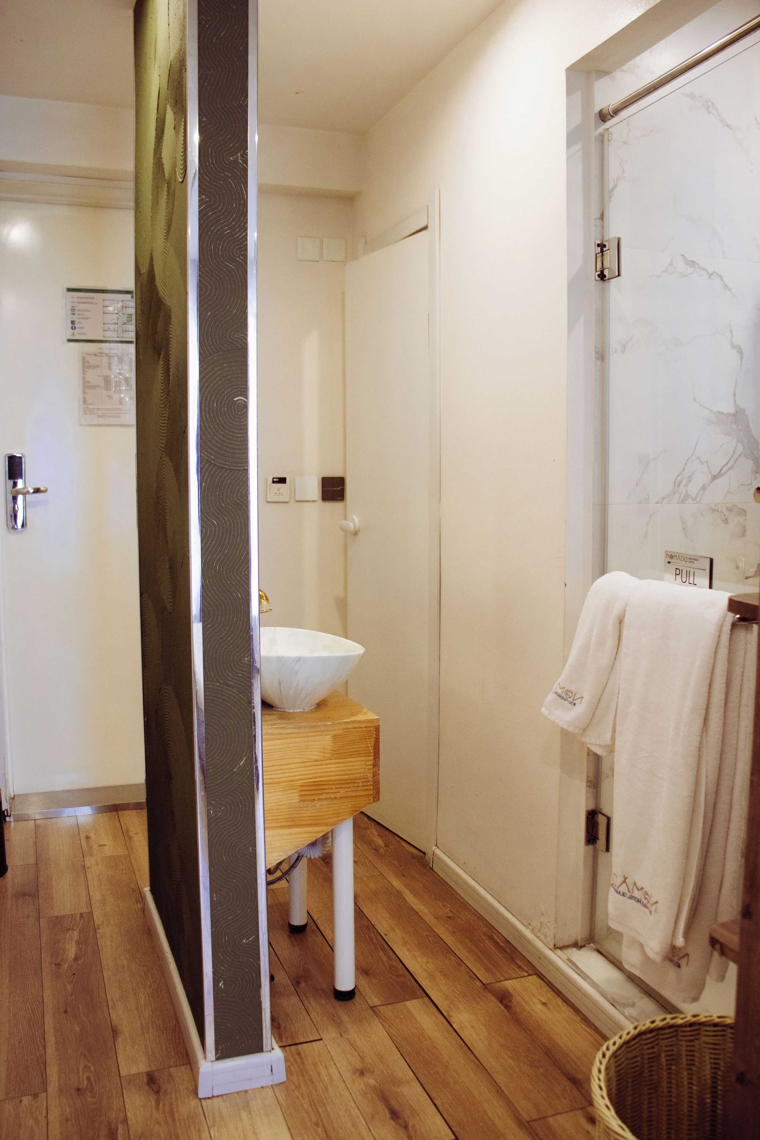 A bathroom with a wooden floor, a white sink, a glass shower enclosure, and a towel rack.