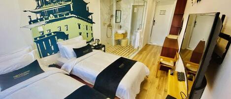 A hotel room with two beds, a bathroom with a glass shower, a wooden floor, and a TV on a stand.