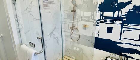 Ducha con cerramiento de vidrio, estante de madera, perchero y una mesita con tetera.