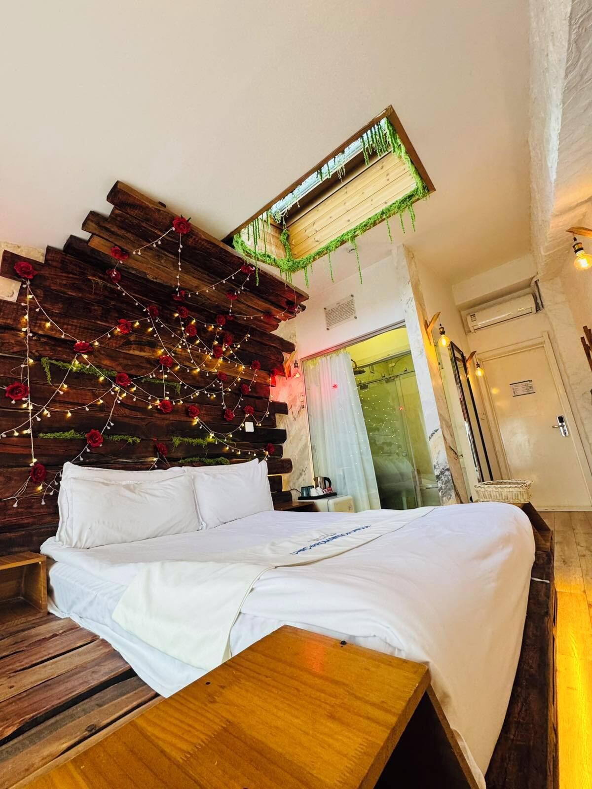 Una cama con ropa blanca, cabecera de madera y luces de hadas con rosas rojas.