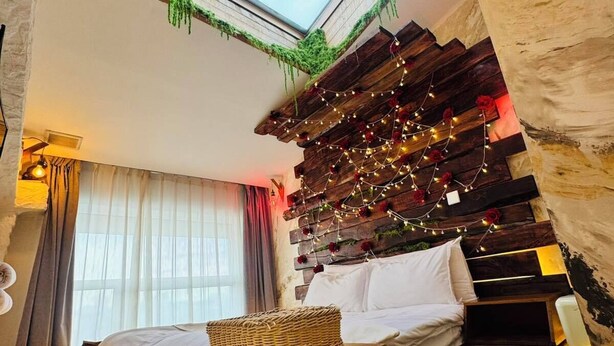 Ein Schlafzimmer mit Oberlicht, Holzbettgestell, Lichterkette und Blick ins Freie.