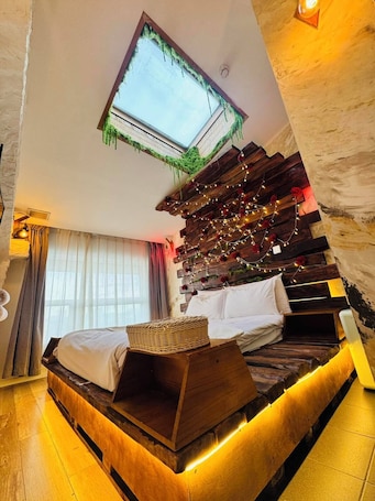 A bedroom with a skylight, wooden bed frame, string lights, and a view of the outdoors.