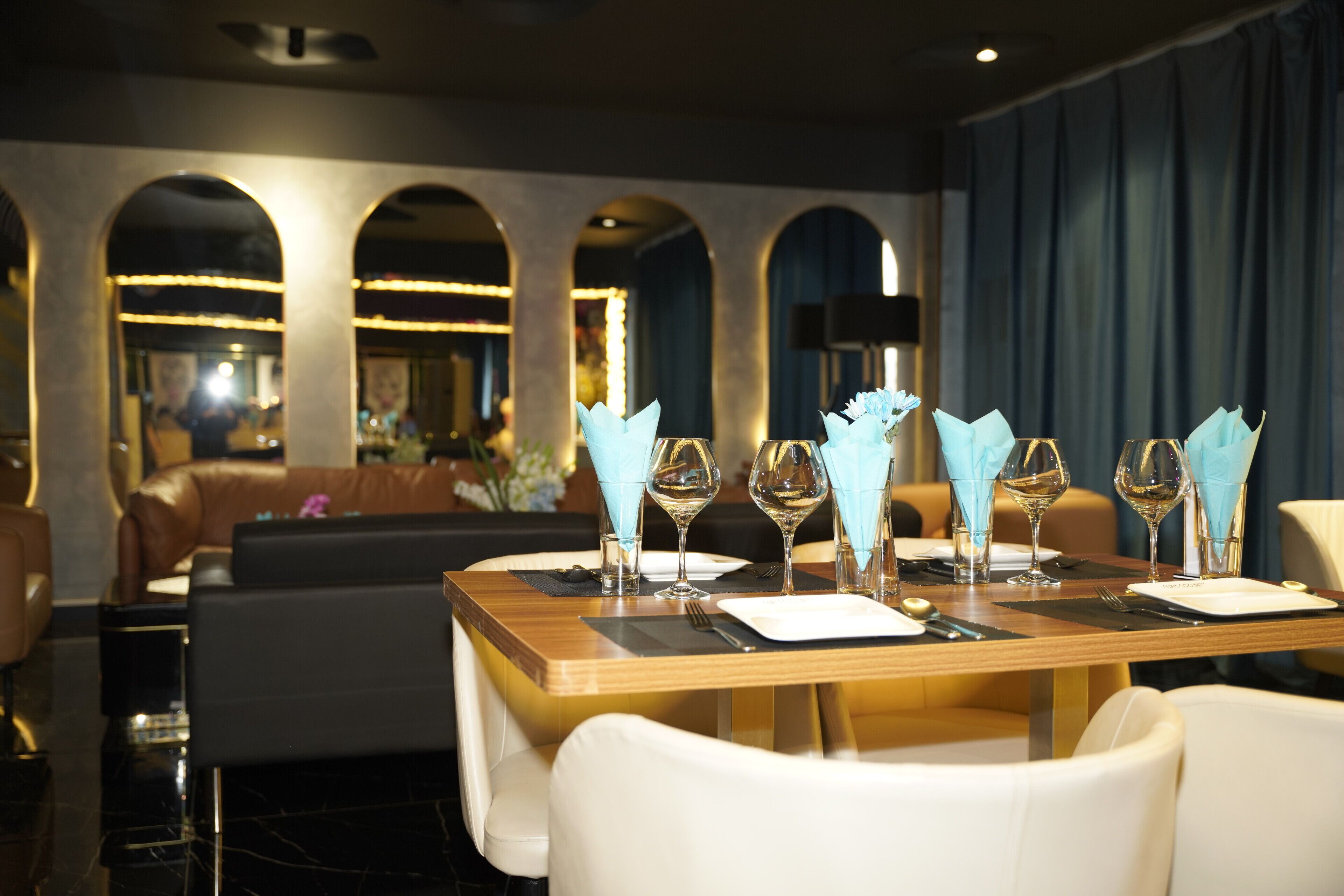 Un comedor con una mesa de madera dispuesta para dos personas, sillas blancas y servilletas azules.