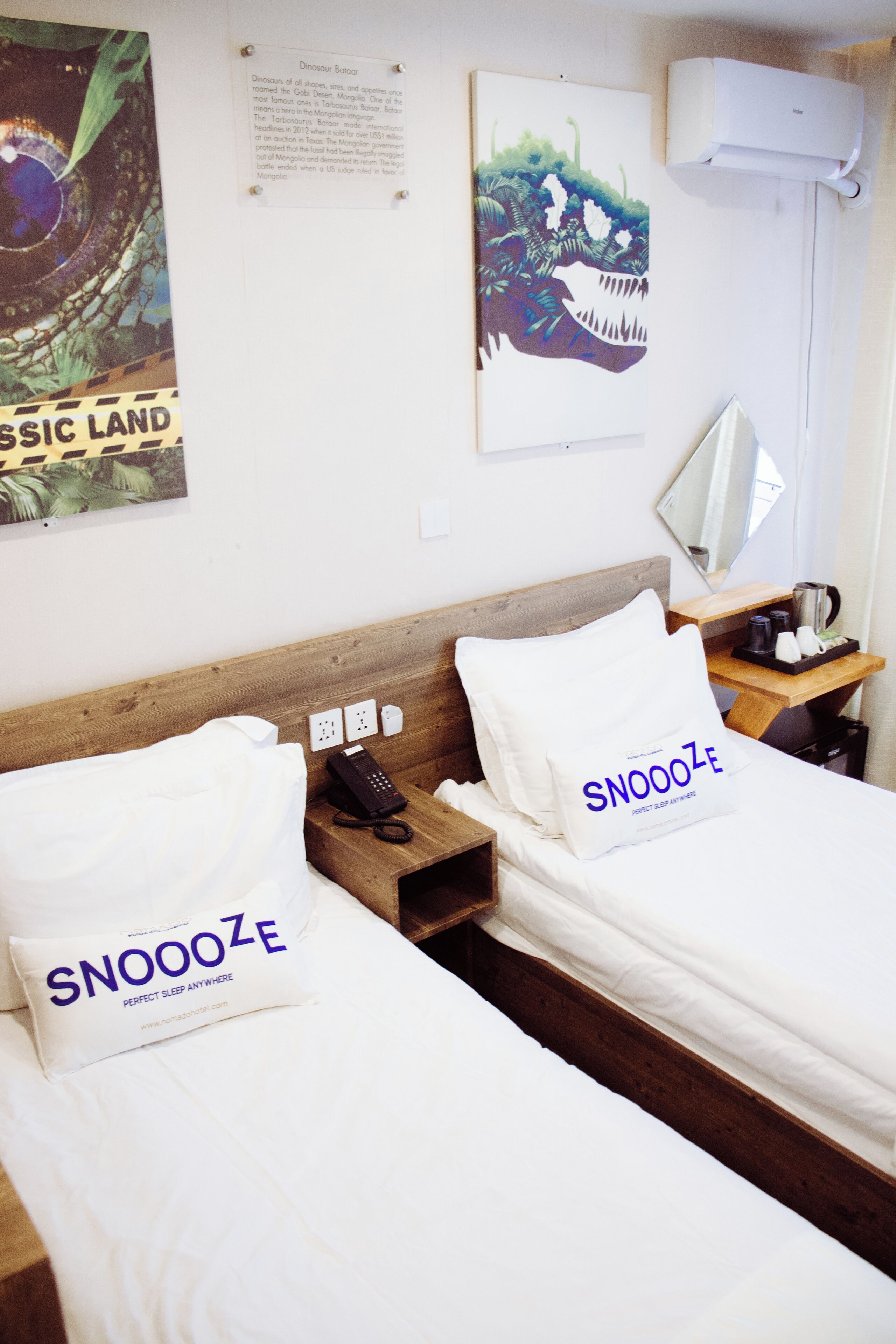 Una camera d'albergo con due letti, un comodino con il telefono, uno specchio e un quadro appeso al muro.