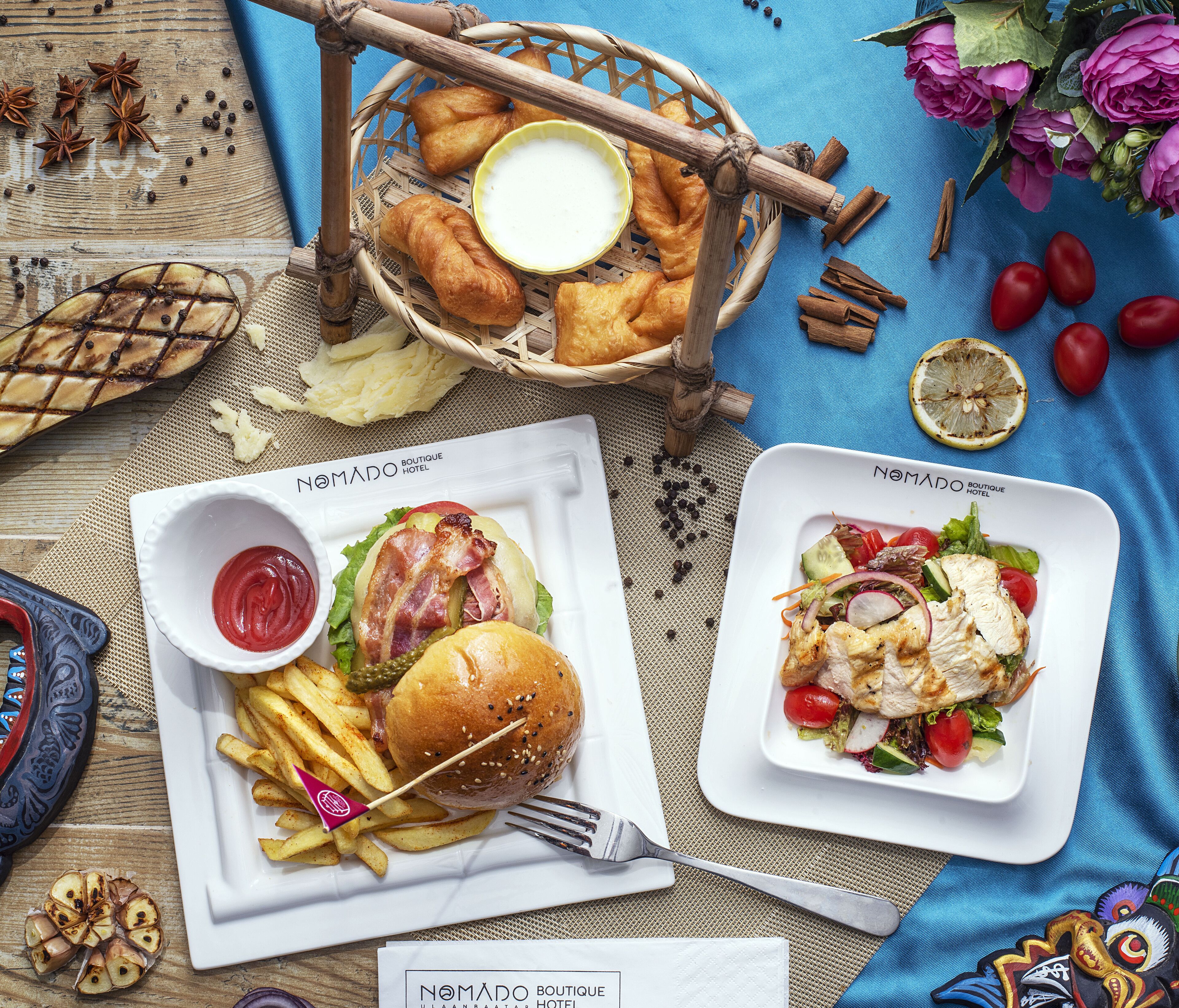 A dining table with a basket of bread, a plate of fries with a burger, a plate of salad, and a bowl of ketchup.