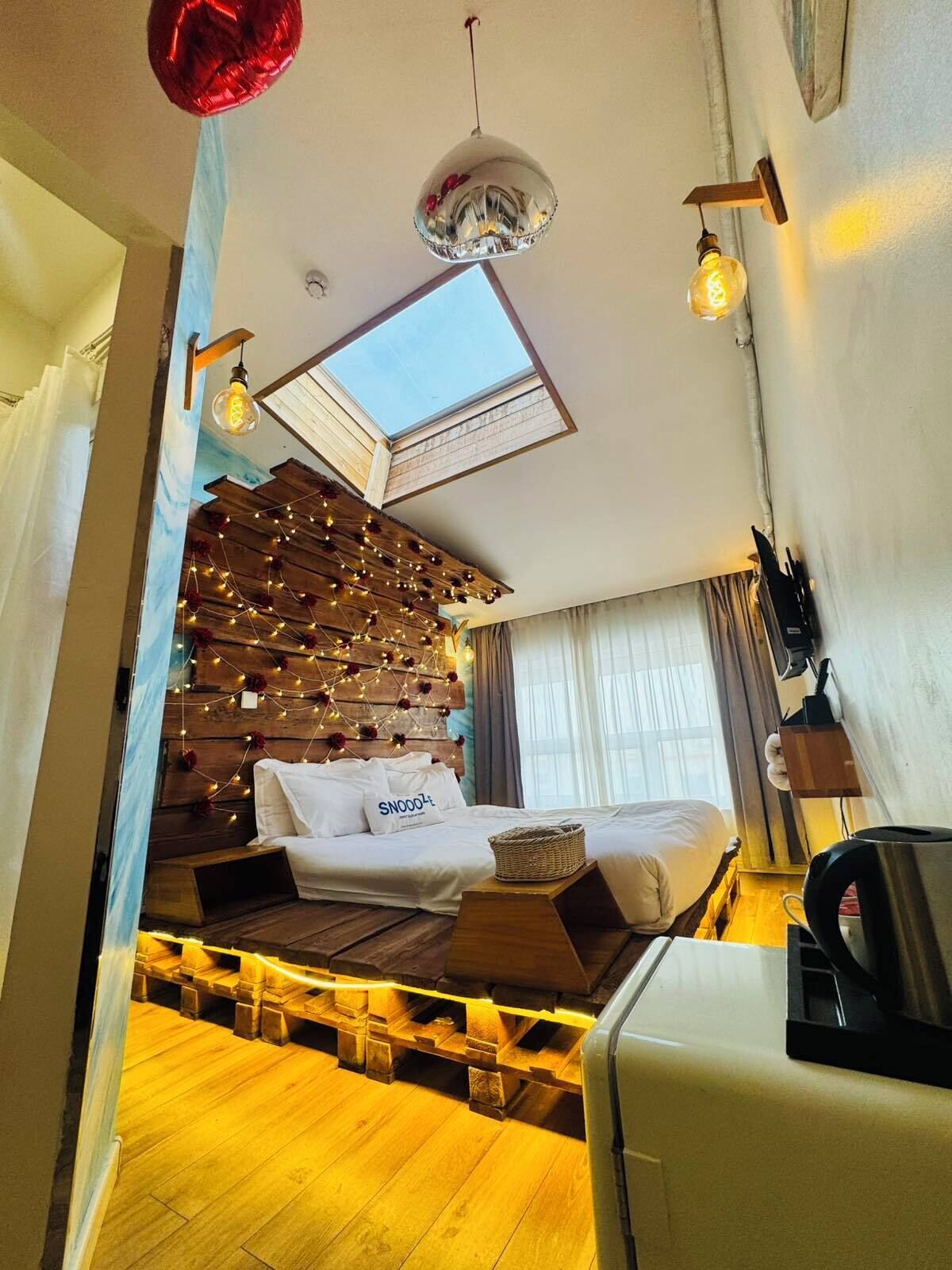 Habitación de hotel moderna con pared de madera, una cama, tragaluz y cafetera.