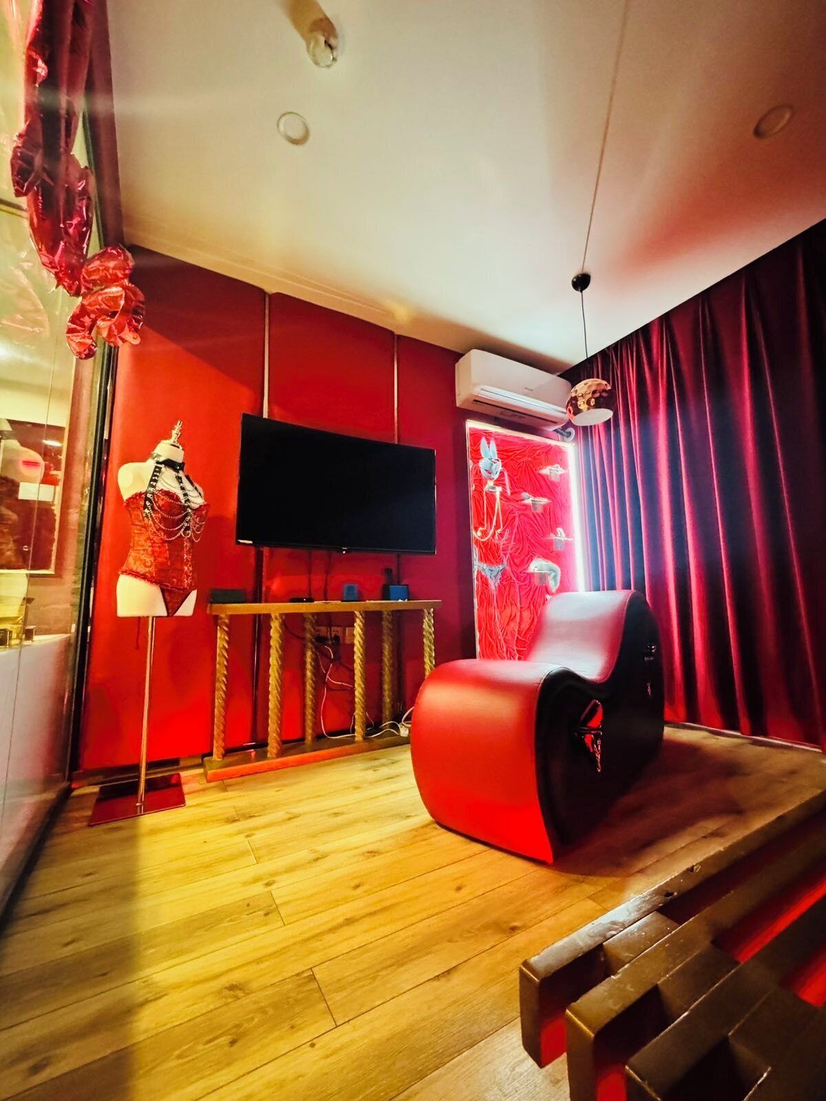 A modern living room with a flat-screen TV, a red sofa, and a mannequin in a red outfit.