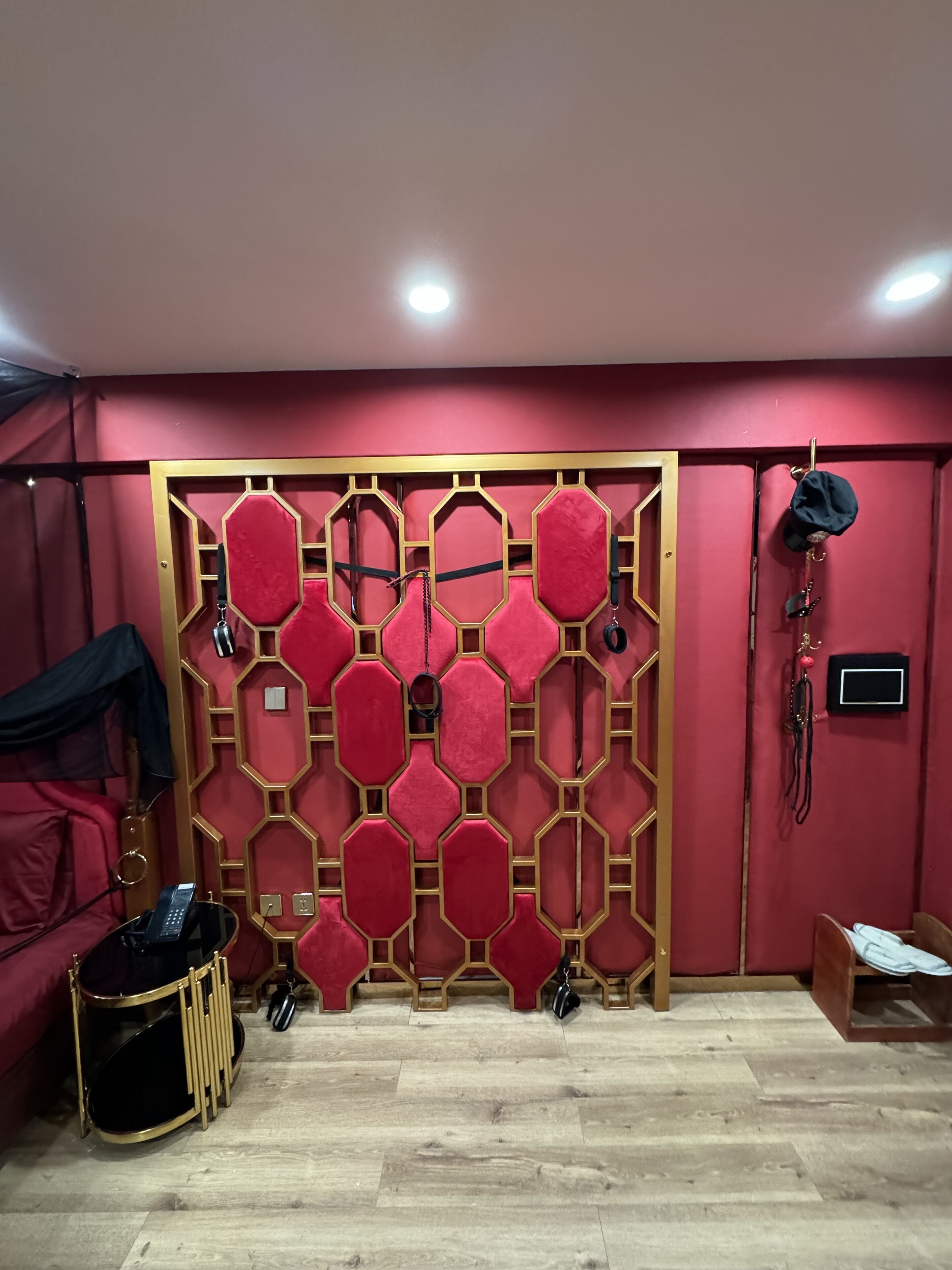 A room with a red and gold geometric wall panel, a black telephone, and a wooden floor.