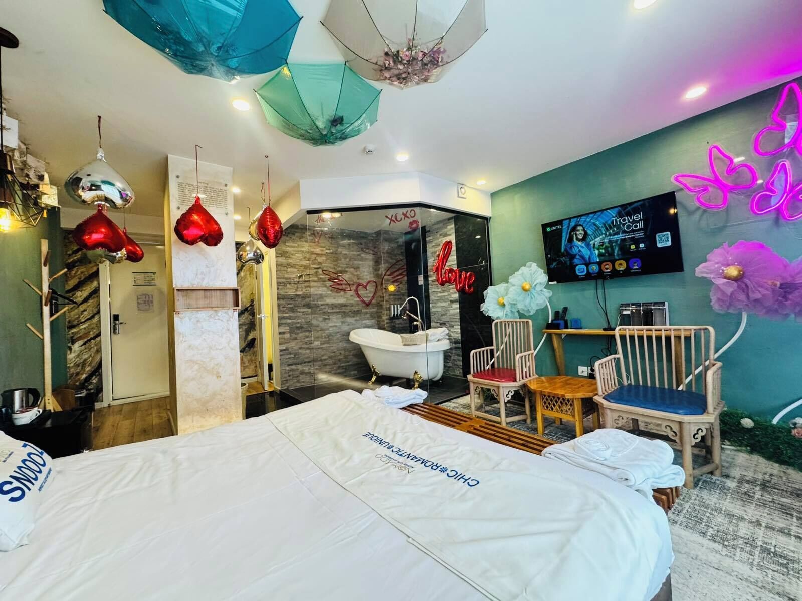 A hotel room with a bed, a shower area, a TV, and a neon sign.